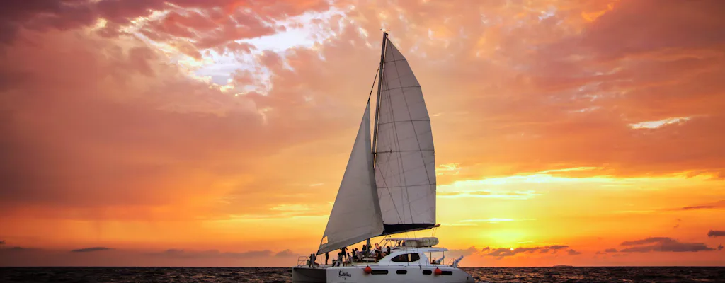 Luxury catamaran sailing off Cancun beneath an orange sunset sky
